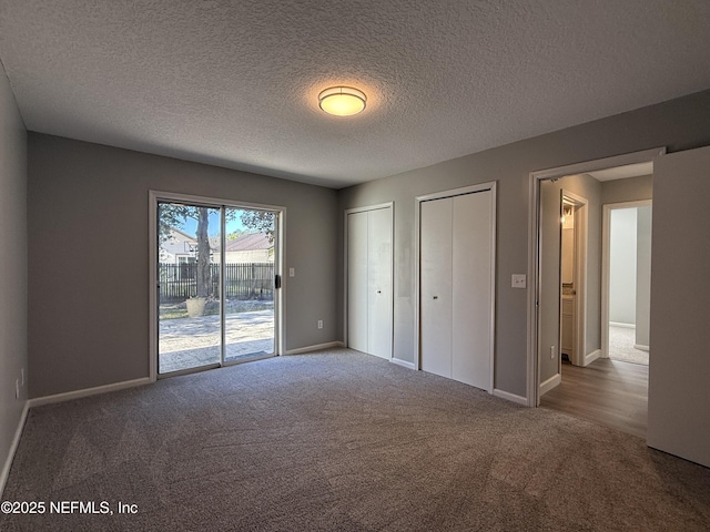 unfurnished bedroom with dark carpet, a textured ceiling, access to outside, and multiple closets