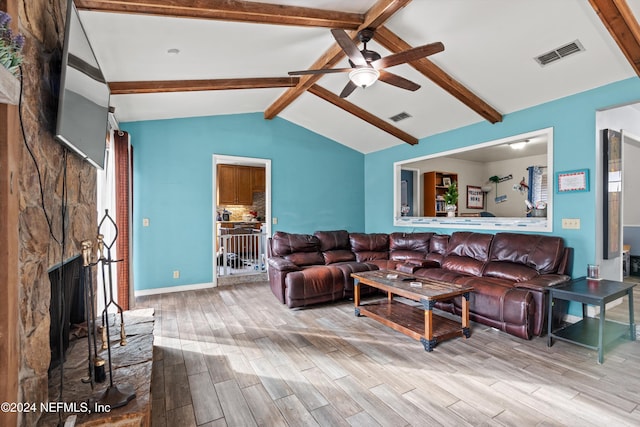 living room with vaulted ceiling with beams, ceiling fan, a stone fireplace, and light wood-type flooring