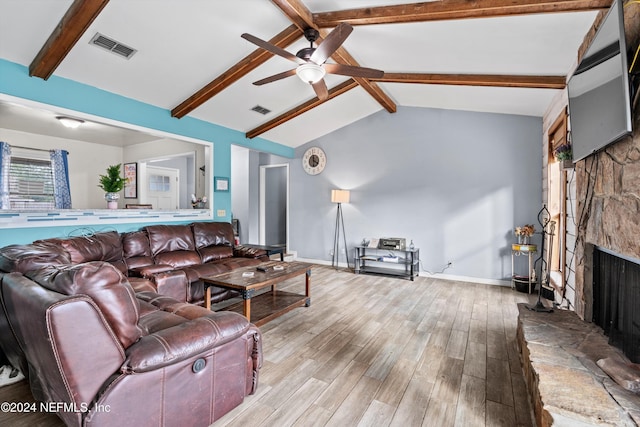 living room with lofted ceiling with beams, ceiling fan, a stone fireplace, and light wood-type flooring