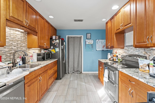 kitchen with light stone countertops, appliances with stainless steel finishes, tasteful backsplash, and sink