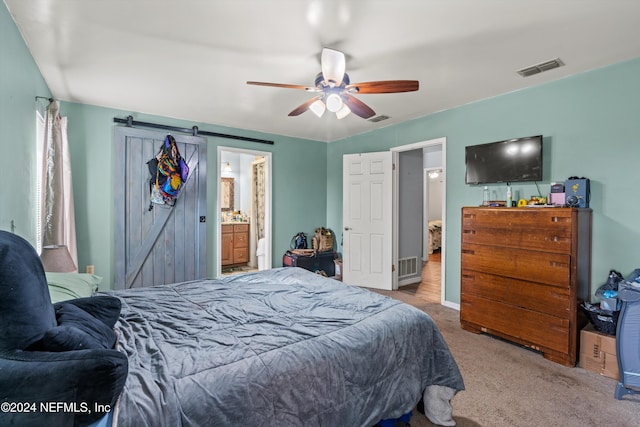 carpeted bedroom with ensuite bath, ceiling fan, and a barn door