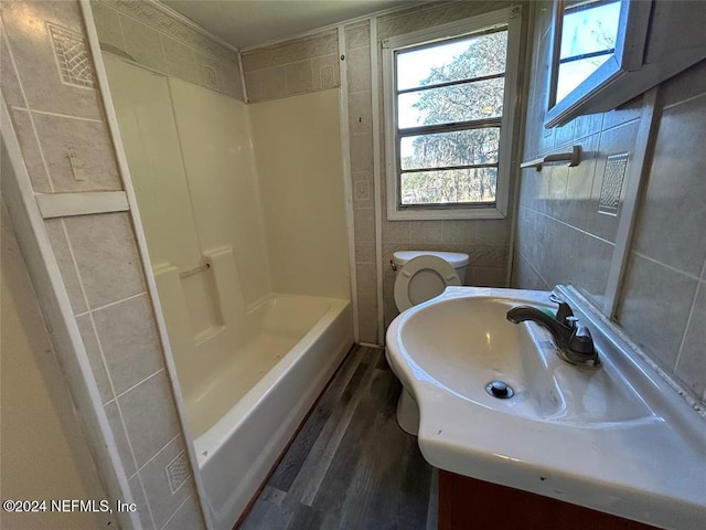 full bathroom featuring hardwood / wood-style floors, toilet, shower / tub combination, vanity, and tile walls