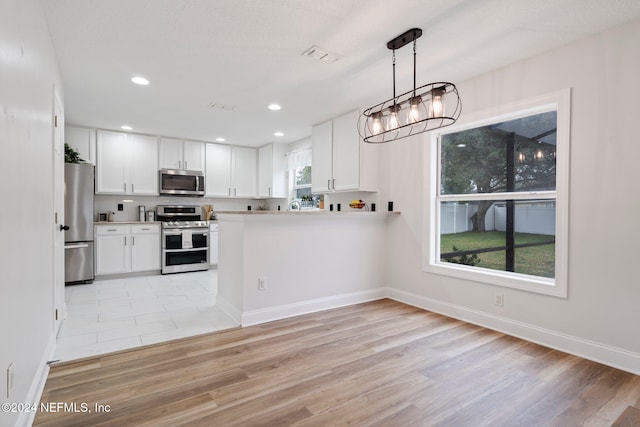 kitchen with pendant lighting, white cabinets, light wood-type flooring, and appliances with stainless steel finishes