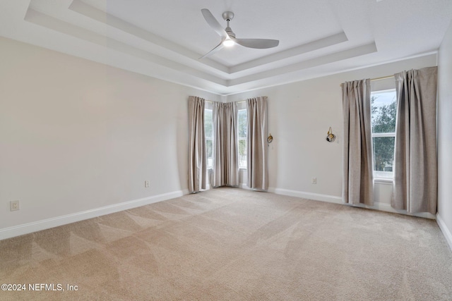 carpeted spare room featuring a tray ceiling, ceiling fan, and plenty of natural light