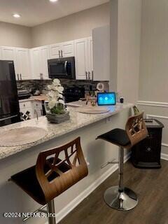 kitchen with light stone counters, dark hardwood / wood-style flooring, a breakfast bar area, white cabinets, and black appliances