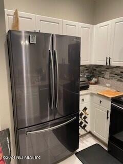 kitchen featuring backsplash, stainless steel refrigerator, white cabinets, and black / electric stove