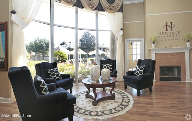 living room with wood-type flooring, crown molding, a towering ceiling, and a tiled fireplace