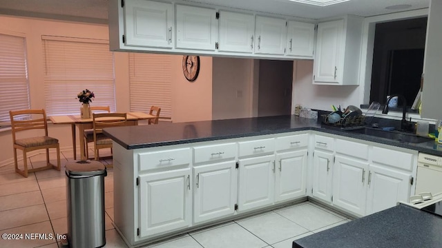 kitchen with kitchen peninsula, white dishwasher, sink, light tile patterned floors, and white cabinetry