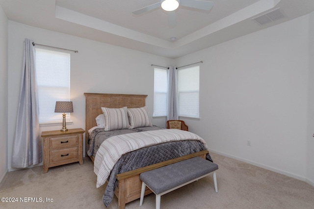 carpeted bedroom featuring a raised ceiling, multiple windows, and ceiling fan