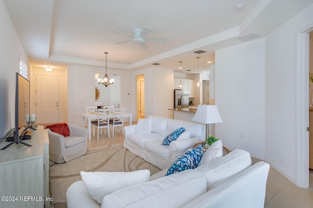 living room with a tray ceiling and ceiling fan with notable chandelier