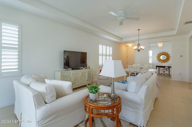 living room featuring ceiling fan with notable chandelier, light tile patterned floors, and a tray ceiling