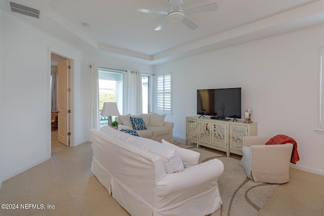 living room with a tray ceiling, ceiling fan, and light tile patterned floors