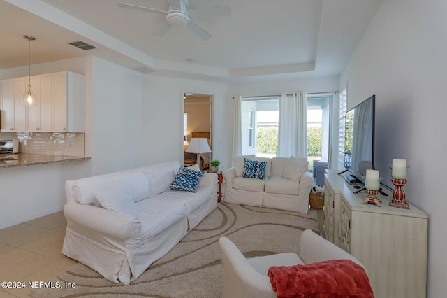 living room featuring a raised ceiling, ceiling fan, and light tile patterned floors