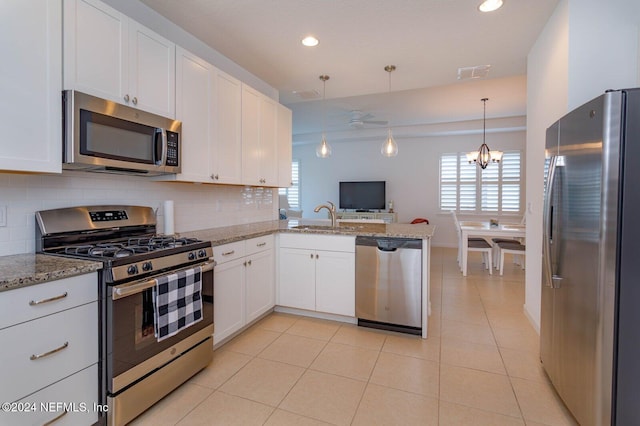 kitchen with kitchen peninsula, appliances with stainless steel finishes, tasteful backsplash, decorative light fixtures, and white cabinetry