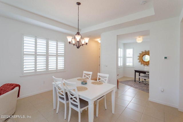 dining space with a tray ceiling, light tile patterned floors, a wealth of natural light, and an inviting chandelier