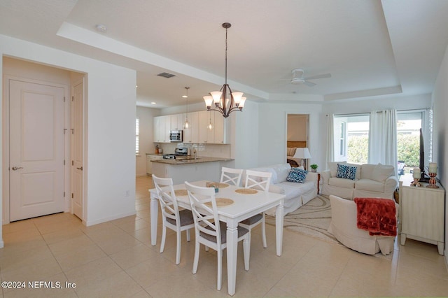 dining room featuring ceiling fan with notable chandelier and a tray ceiling