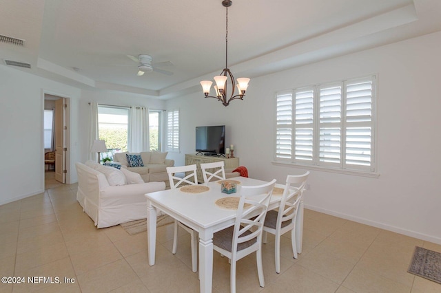 tiled dining area featuring ceiling fan with notable chandelier and a raised ceiling