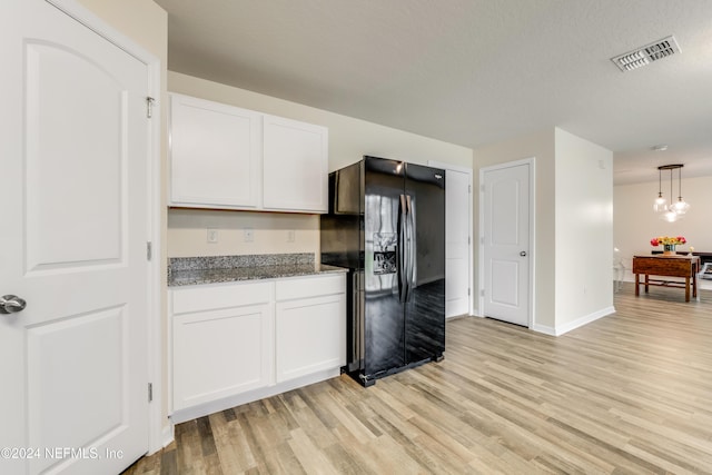 kitchen with white cabinets, light hardwood / wood-style flooring, and black fridge