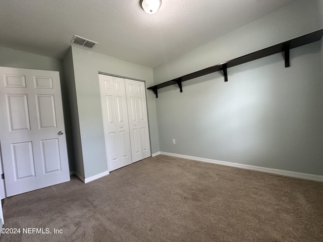 unfurnished bedroom featuring a closet, a textured ceiling, and dark colored carpet