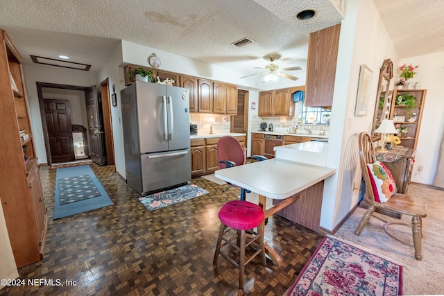 kitchen featuring a kitchen bar, kitchen peninsula, stainless steel appliances, and a textured ceiling