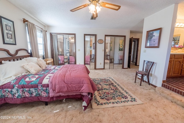 bedroom featuring two closets, ceiling fan, a textured ceiling, connected bathroom, and light colored carpet