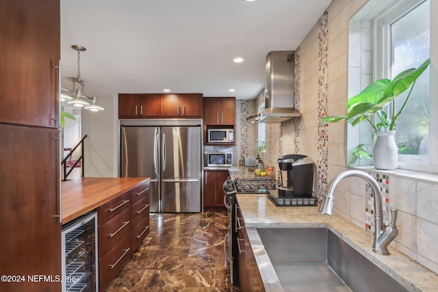 kitchen featuring sink, wall chimney exhaust hood, stainless steel appliances, beverage cooler, and pendant lighting