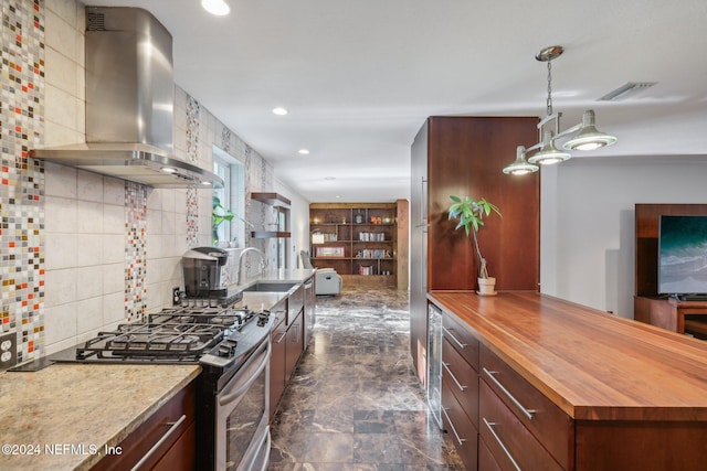 kitchen featuring pendant lighting, backsplash, wall chimney range hood, gas range, and butcher block counters