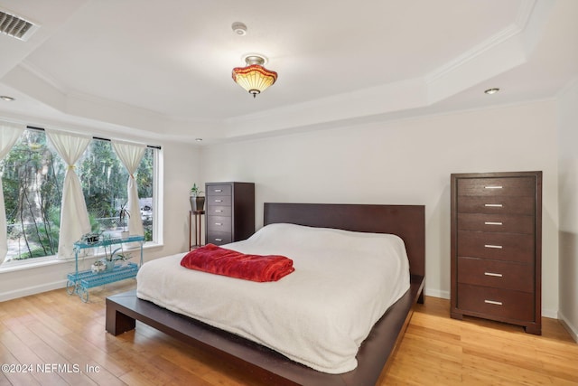 bedroom with crown molding, light hardwood / wood-style flooring, and a tray ceiling