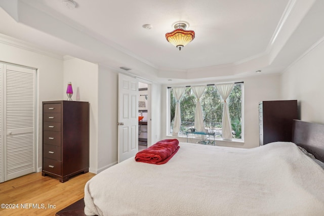 bedroom with light hardwood / wood-style floors, crown molding, and a tray ceiling