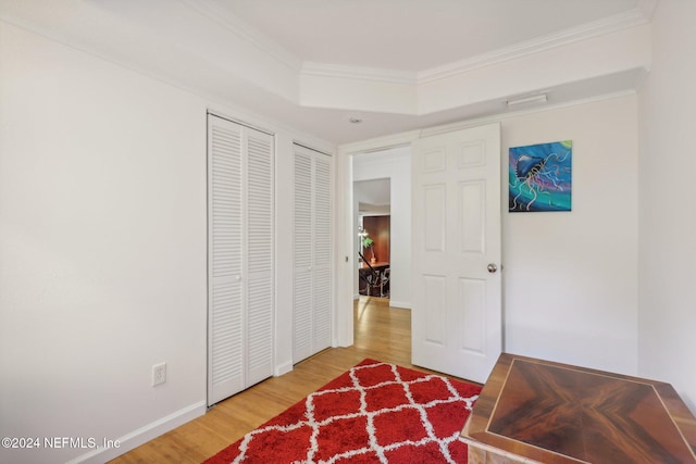 bedroom with wood-type flooring, two closets, and ornamental molding