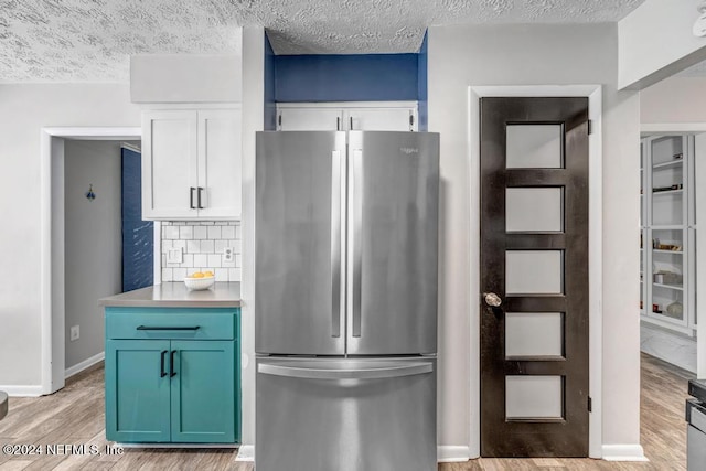 kitchen with white cabinets, a textured ceiling, light wood-type flooring, and stainless steel refrigerator