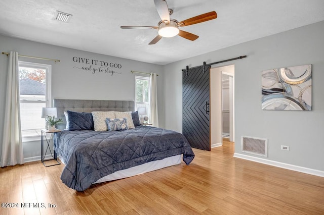 bedroom featuring a barn door, ceiling fan, and light hardwood / wood-style flooring