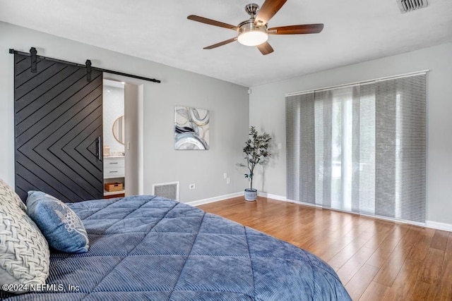 bedroom featuring ceiling fan, a barn door, and wood-type flooring