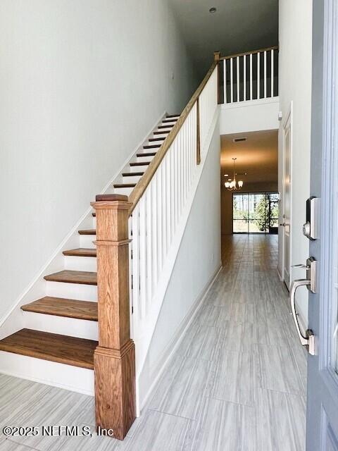 stairs with a towering ceiling, hardwood / wood-style floors, and a chandelier