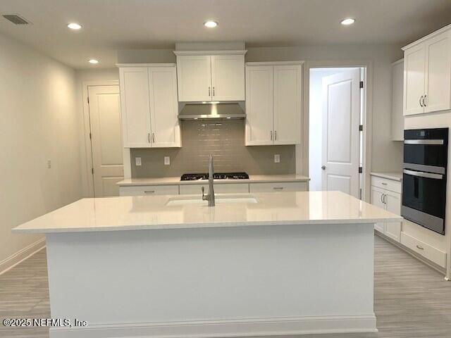 kitchen with white cabinetry, decorative backsplash, a center island with sink, and light hardwood / wood-style flooring