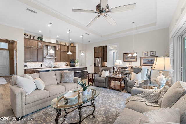 living room featuring ceiling fan, a raised ceiling, light wood-type flooring, and crown molding