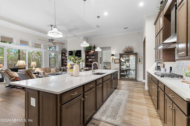 kitchen featuring a center island with sink, wall chimney range hood, sink, hanging light fixtures, and ceiling fan