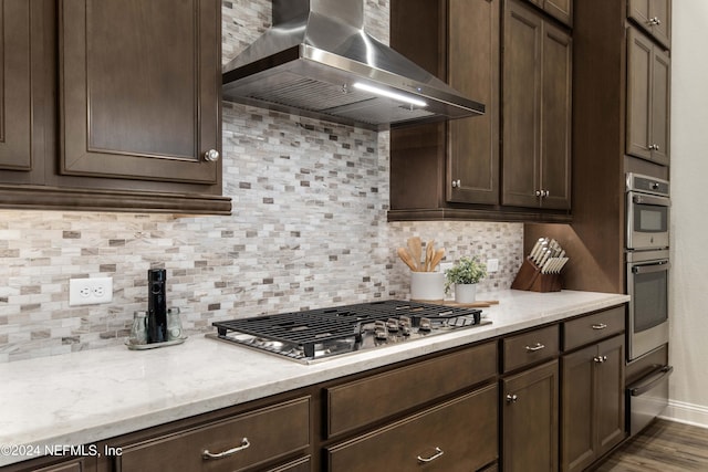 kitchen with wall chimney exhaust hood, dark brown cabinetry, decorative backsplash, and appliances with stainless steel finishes