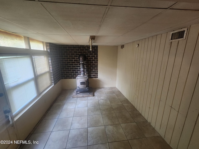 spare room with tile patterned floors, a paneled ceiling, a wood stove, and wooden walls