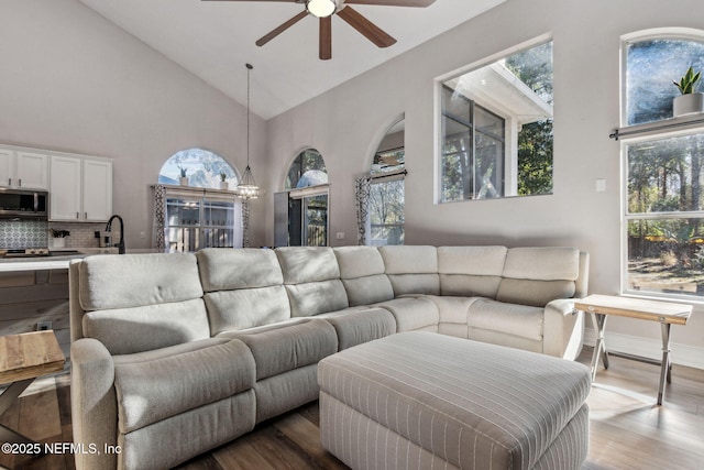 living room featuring hardwood / wood-style flooring, ceiling fan with notable chandelier, and high vaulted ceiling