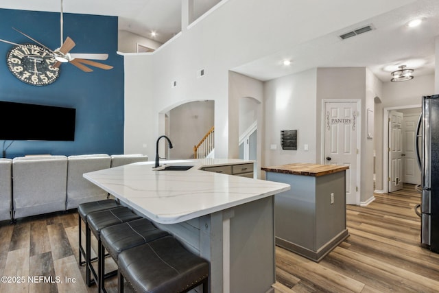 kitchen featuring a kitchen bar, sink, wood-type flooring, a center island with sink, and high vaulted ceiling