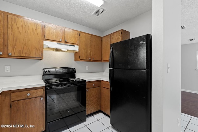 kitchen with light tile patterned flooring, black appliances, and a textured ceiling