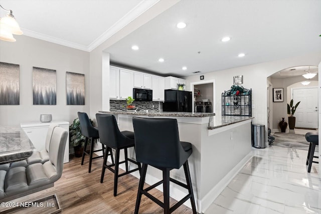 kitchen featuring kitchen peninsula, white cabinetry, a breakfast bar area, and black appliances