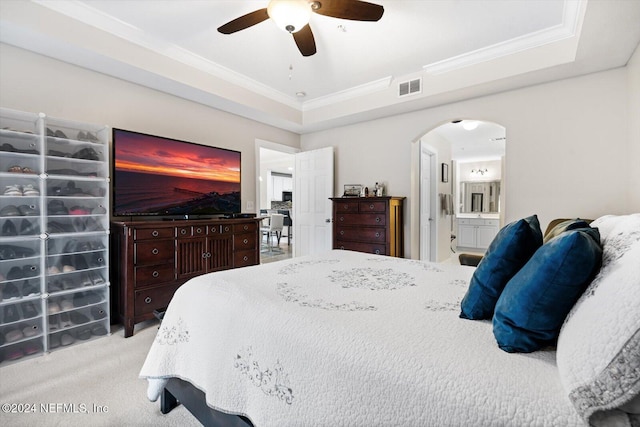 bedroom featuring light carpet, ensuite bathroom, a tray ceiling, ceiling fan, and crown molding