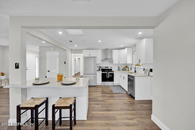 kitchen featuring appliances with stainless steel finishes, a kitchen breakfast bar, tasteful backsplash, wall chimney exhaust hood, and white cabinets