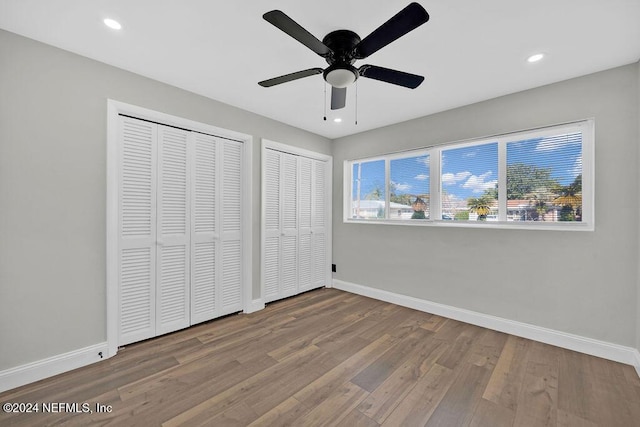 unfurnished bedroom featuring multiple closets, ceiling fan, and hardwood / wood-style floors