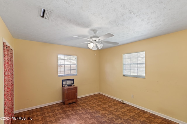 spare room with a wealth of natural light, dark parquet floors, ceiling fan, and a textured ceiling