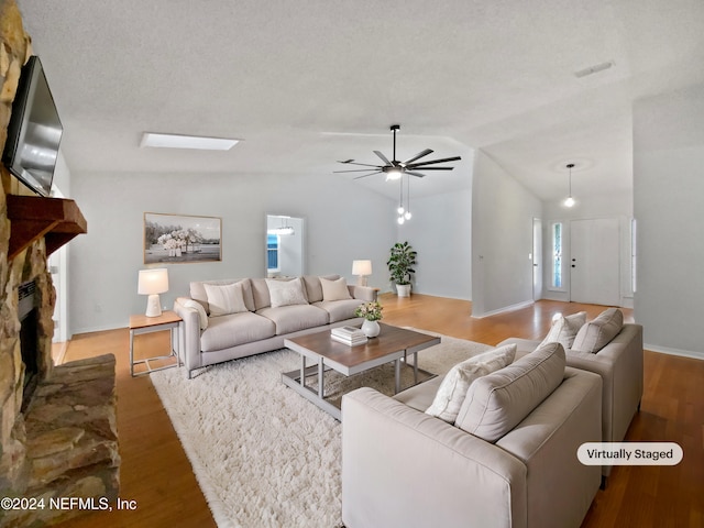 living room with ceiling fan, hardwood / wood-style floors, a textured ceiling, lofted ceiling, and a fireplace