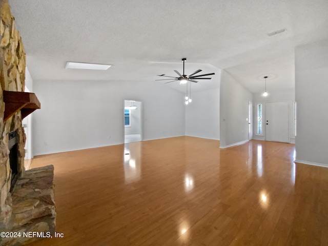 unfurnished living room with light wood-type flooring, a textured ceiling, vaulted ceiling, ceiling fan, and a fireplace