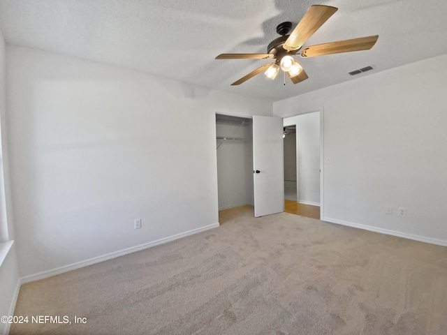 unfurnished bedroom with light carpet, a textured ceiling, a closet, and ceiling fan